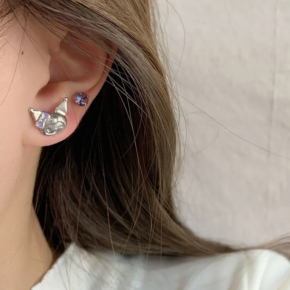 Boucles d'oreilles asymétriques Kuromi argentées avec strass violets portées par une femme. Gros plan sur son oreille. Un bijou kawaii inspiré de l'univers japonais, idéal pour compléter une tenue ou offrir en cadeau.