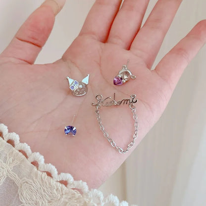 Boucles d'oreilles asymétriques Kuromi argentées avec strass violets et chaîne décorative, posées dans une main de femme. Un bijou kawaii inspiré de l'univers japonais, idéal pour compléter une tenue ou offrir en cadeau.