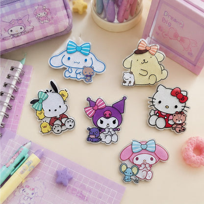 Magnets pailletés kawaii représentant plusieurs personnages Sanrio : Kuromi, cinnamoroll, Pompompurin, Hello Kitty, Pochacco et My Melody, placés sur un bureau d'écolière kawaii aux tons pastel, avec stylos roses, carnets et trousses pastels. Ambiance douce, chaleureuse et féminine.
