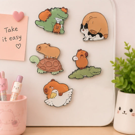 Des magnets kawaii représentant un capybara, un crocodile, un chat et un goéland sont aimantés sur un support blanc. Dans un décor doux et apaisant et une ambiance calme.