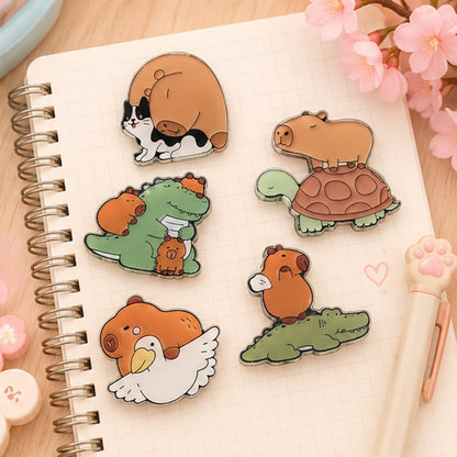 Des magnets kawaii représentant un capybara, un crocodile, un chat et un goéland sont posés sur un carnet de notes ouvert, sur un bureau mignon. Ambiance douce, dans un décor rose pastel mignon.