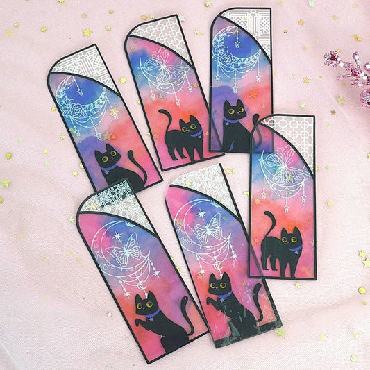 des marque-pages façon vitrail coloré orné de papillons ou de lunes. Un adorable chat noir se trouve devant. L'ensemble est mystérieux et magique.