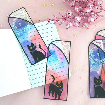 des marque-pages façon vitrail coloré orné de papillons ou de lunes. Un adorable chat noir se trouve devant. L'ensemble est mystérieux et magique.