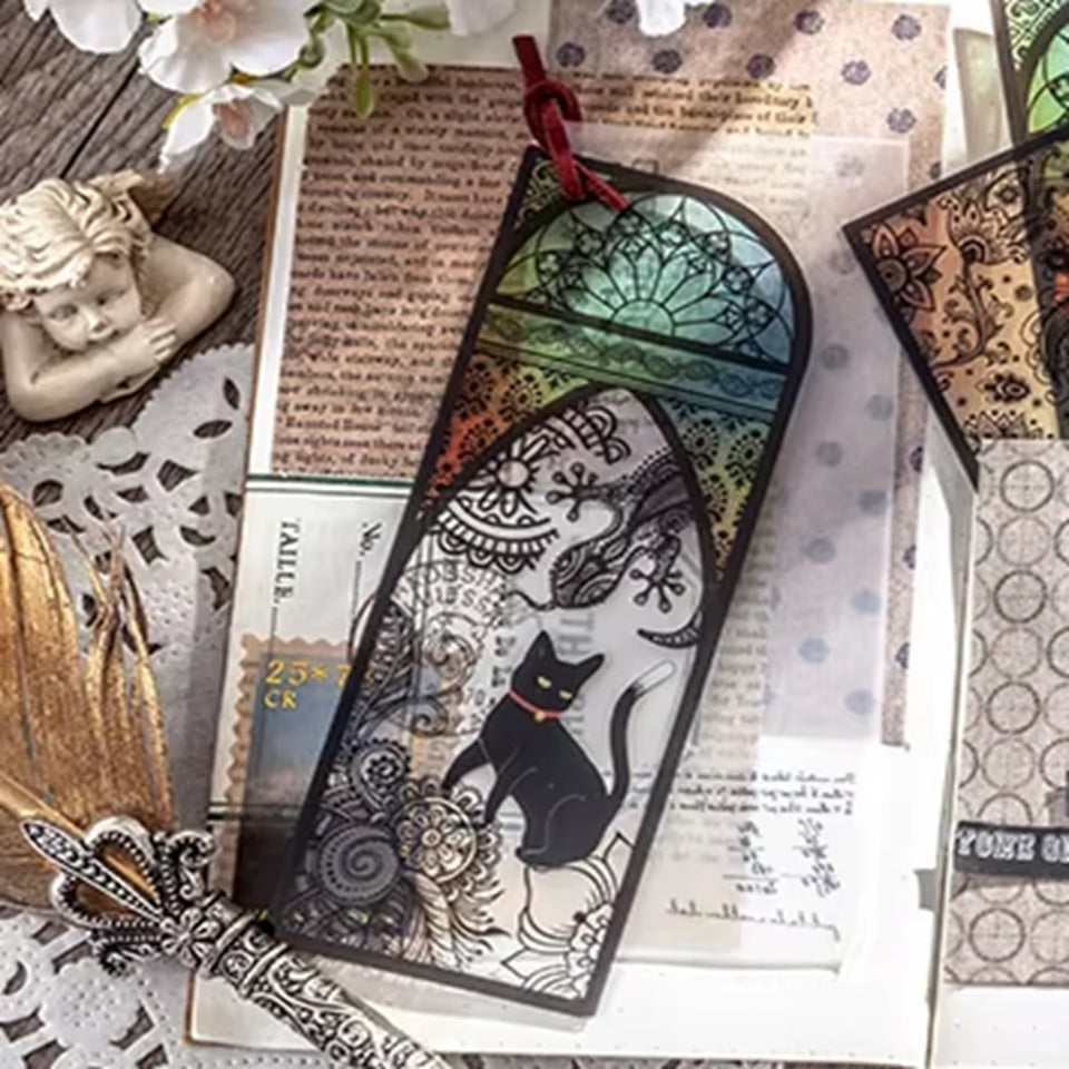 des marque-pages façon vitrail coloré orné de papillons ou de lunes. Un adorable chat noir se trouve devant. L'ensemble est mystérieux et magique.