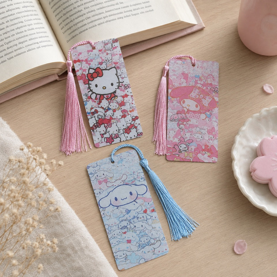 Marque-pages kawaii Hello Kitty, My Melody et Cinnamoroll avec pompons colorés, présentés sur un bureau en bois clair avec livre ouvert et décoration pastel.