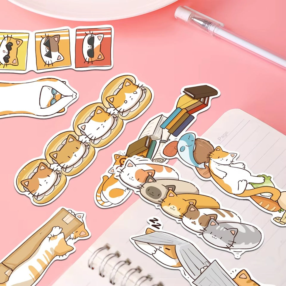 des marques-pages cartonnés représentant des chats bruns, roux et gris dans de situations cocasses et rigolotes posés sur un bureau rose et mignon.