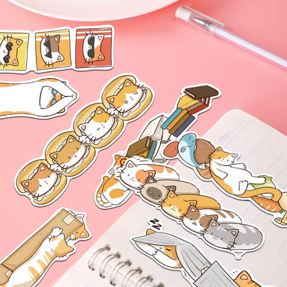 des marques-pages cartonnés représentant des chats bruns, roux et gris dans de situations cocasses et rigolotes posés sur un bureau rose et mignon.