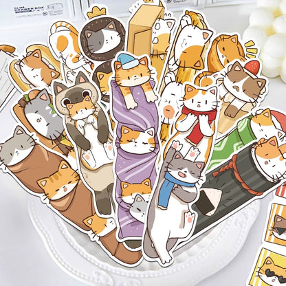 des marques-pages cartonnés représentant des chats bruns, roux et gris dans de situations cocasses et rigolotes Ils sont posés sur une assiette sur une table légèrement décorée.