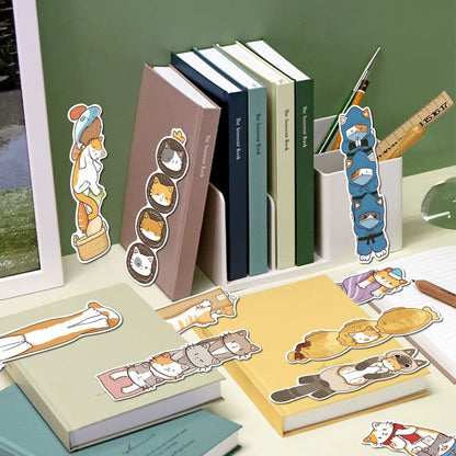 des marques-pages cartonnés représentant des chats bruns, roux et gris dans de situations cocasses et rigolotes. Ils sont posés sur différents livres de couleurs.