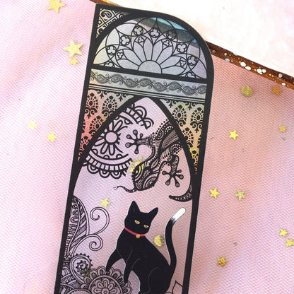 des marque-pages façon vitrail coloré orné de papillons ou de lunes. Un adorable chat noir se trouve devant. L'ensemble est mystérieux et magique.