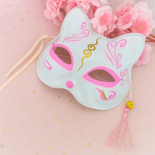 un masque kitsune rose avec des détails dorés, pompons et clochettes. Idéal pour un cosplay, une soirée déguisée ou en décoration.