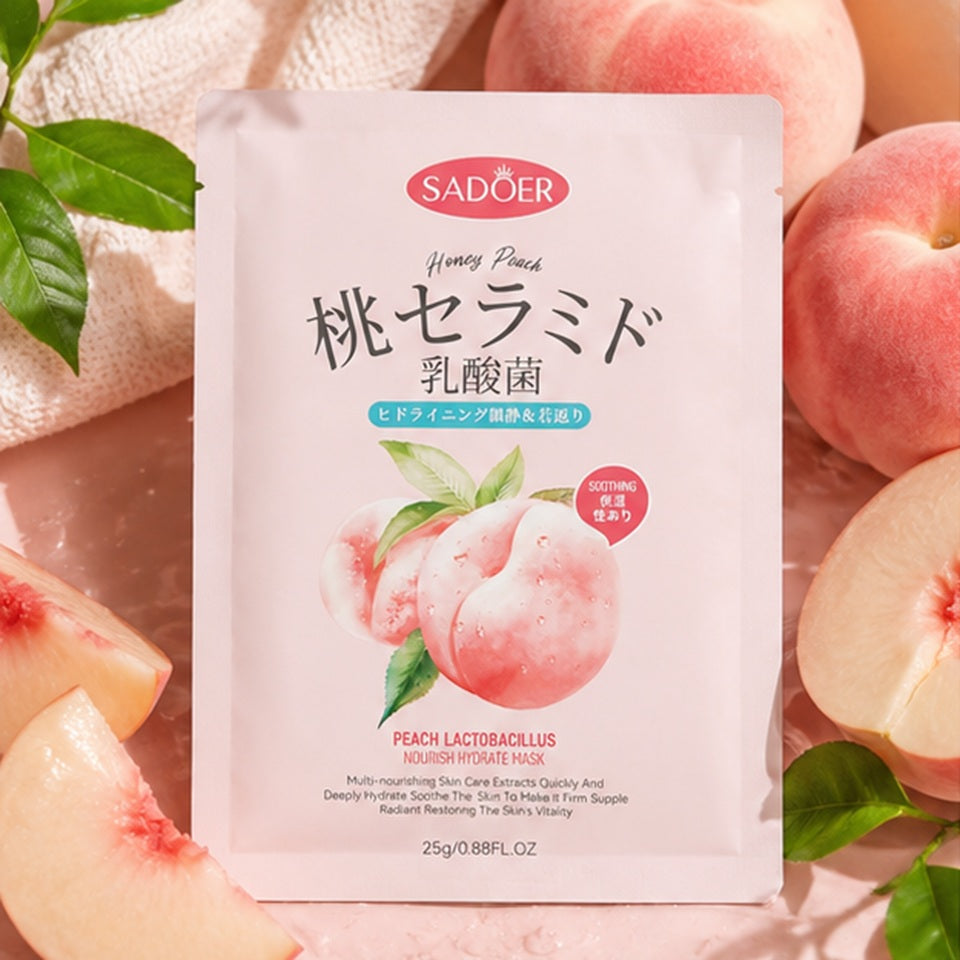 Sachet de masque visage à la pêche SADOER posé au milieu de pêches fraîches et de tranches de pêche, sur un fond rose pastel. La composition met en avant l'univers fruité et rafraîchissant du soin dans une ambiance chaleureuse et estivale.