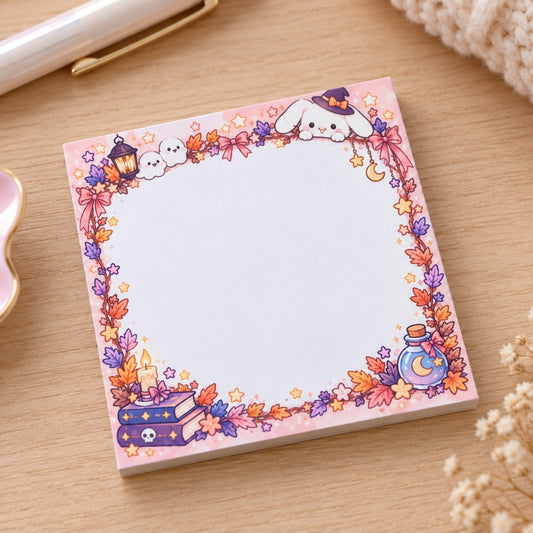 Bloc mémo carré kawaii Halloween aux tons rose et violet pastel, décoré de lapins sorciers, citrouilles, fantôme, chauves-souris, livres et potions magiques. Il y a une grande zone blanche pour écrire ses notes et rappels.
