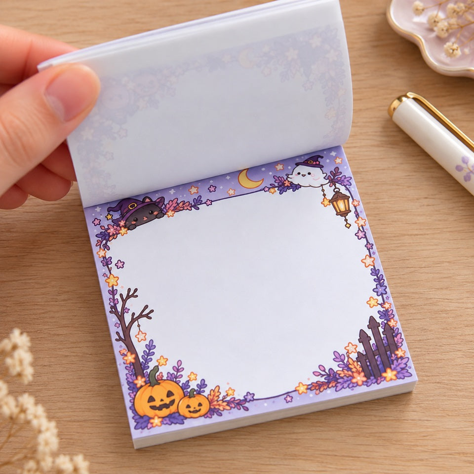 Bloc mémo kawaii Halloween aux couleurs pastel, décoré d’un chat sorcier, d’un petit fantôme, de citrouilles et d’étoiles. Une main soulève les feuilles pour dévoiler l’espace d’écriture blanc.