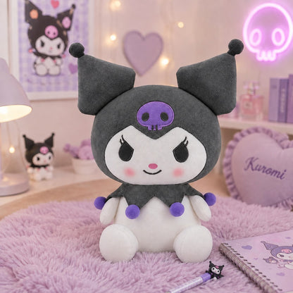 Peluche Kuromi kawaii noire et blanche avec tête de mort violette et pompons colorés, présentée dans un joli décor de chambre pastel rose et lilas.