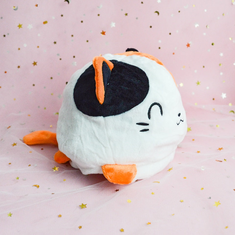 une peluche en forme de chat de culeur calico réversible. On peut la retourner pour montrer notre expression : heureuse ou plutôt fâchée