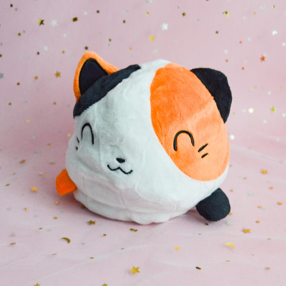 une peluche en forme de chat de culeur calico réversible. On peut la retourner pour montrer notre expression : heureuse ou plutôt fâchée