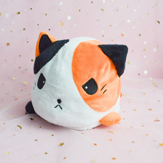 une peluche en forme de chat de culeur calico réversible. On peut la retourner pour montrer notre expression : heureuse ou plutôt fâchée