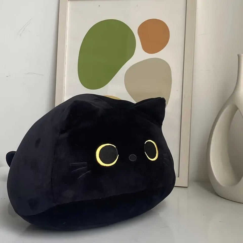 une peluche en forme de chat noir toute ronde et toute câline. Elle a des grands yeux expressifs. Style minimaliste et adorable