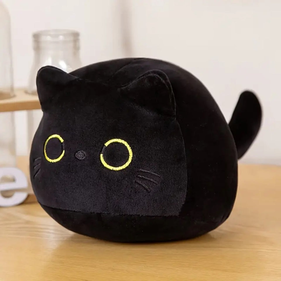une peluche en forme de chat noir toute ronde et toute câline. Elle a des grands yeux expressifs. Style minimaliste et adorable