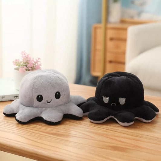 une peluche en forme d'octopus réversible grise et noire qui exprime deux émotions différentes : d'un côté, l'expression heureuse et joyeuse puis quand on le retourne, une expression boudeuse.