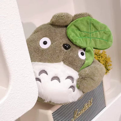 une adorable peluche Totoro qui tient une feuille dans sa main. Adorable et tellement douce, elle est parfaite pour de gros câlins et pour tous les fans.