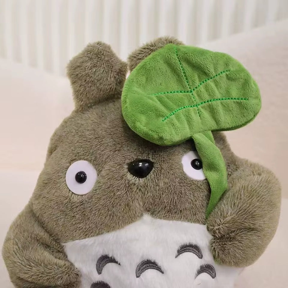 une adorable peluche Totoro qui tient une feuille dans sa main. Adorable et tellement douce, elle est parfaite pour de gros câlins et pour tous les fans.