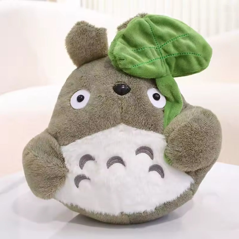 une adorable peluche Totoro qui tient une feuille dans sa main. Adorable et tellement douce, elle est parfaite pour de gros câlins et pour tous les fans.