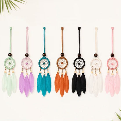 des suspensions attrape-rêves miniatures avec trois plumes, déclinées en plusieurs coloris : vert menthe, rose pastel, bleu turquoise, blanc, noir et orange. Les suspensions sont présentées à plat. Chaque modèle est orné d'un cercle tissé, de perles en bois et de plumes colorées, avec un style bohème et artisanal.
