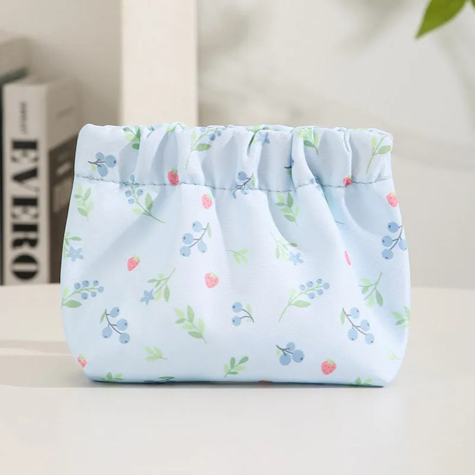 Une pochette de rangement en tissu à motifs floraux pastel bleu, présentée dans un décor lumineux et fleuri.
