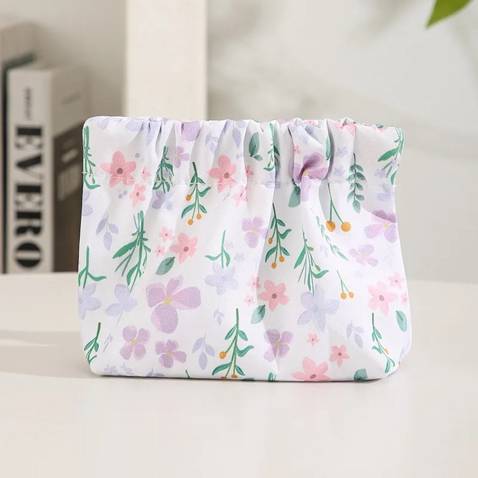 Une pochette de rangement en tissu à motifs floraux pastel mauve et blanc, présentée dans un décor lumineux et fleuri.