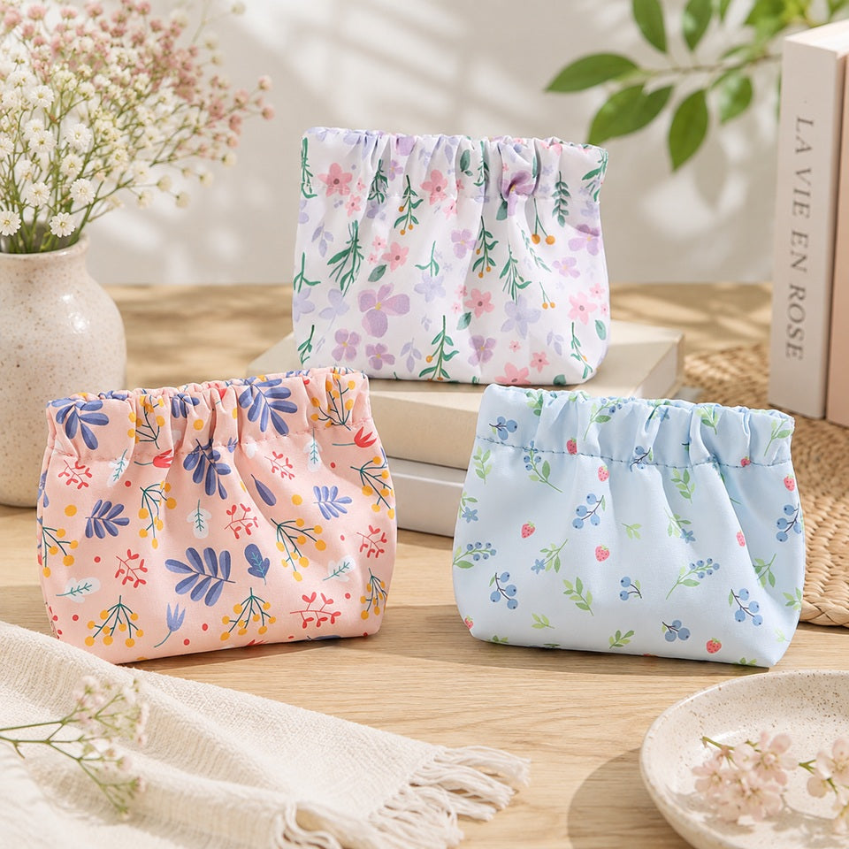 Trois petites pochettes de rangement en tissu à motifs floraux pastel, rose, bleu et blanc, présentées dans un décor lumineux et fleuri.