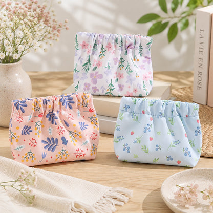 Trois petites pochettes de rangement en tissu à motifs floraux pastel, rose, bleu et blanc, présentées dans un décor lumineux et fleuri.