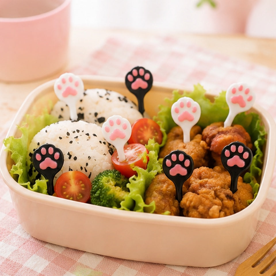Pics décoratifs en forme de pattes de chat roses, noirs et blancs utilisés dans une boîte bento avec riz, légumes et poulet.