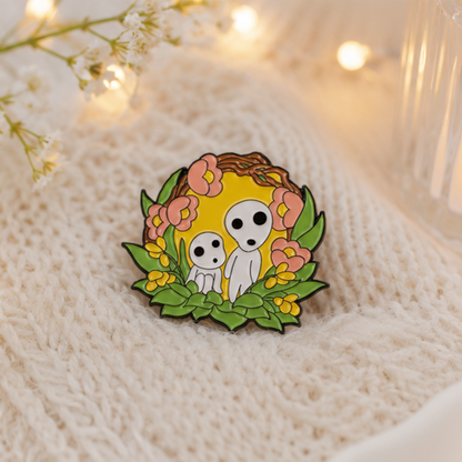 un joli pin's représentant des kodamas, petits êtres mystérieux de la fôret. ils sont dans un décor fleuri et nature