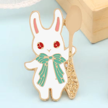 un pin's en forme de lapin blanc aux yeux rouges et qui a un joli noeud papillon vert. Il tient une cuillère dorée.