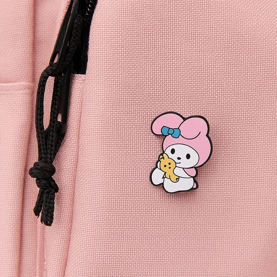 un pin's au design du personnage My Melody de Sanrio. Identifiable grâce à ses longues oreilles roses, il est ici dans une pose trop mignonne avec un petit ourson en peluche dans les mains.