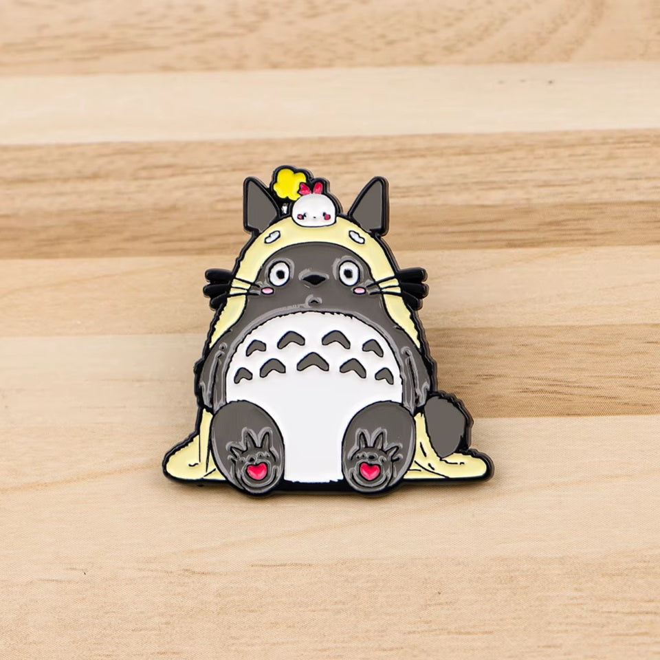 un pin's totoro qui porte une couverture et un petit personnage kawaii trop mignon sur la tête