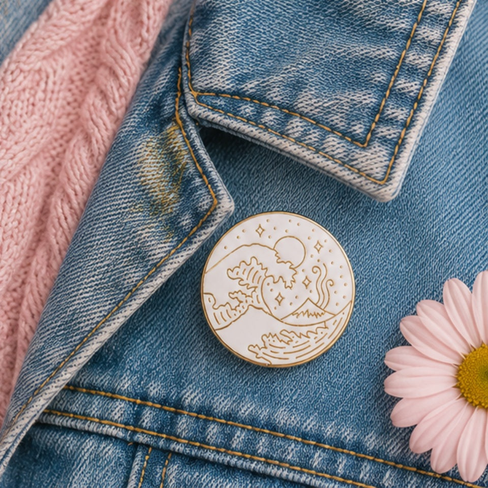 Pin’s vague japonaise minimaliste blanc et doré accroché sur une veste en jean ✨ Badge élégant inspiré de la Grande Vague de Kanagawa avec détails raffinés représentant les vagues, le mont Fuji et un ciel étoilé. Parfait pour personnaliser une veste, un sac ou une tenue avec une touche japonaise chic et poétique.