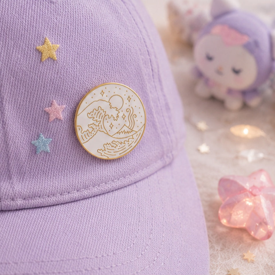 Pin’s vague japonaise minimaliste blanc et doré porté sur une casquette violette pastel ✨ Badge élégant inspiré de la Grande Vague de Kanagawa avec détails raffinés représentant les vagues, le mont Fuji et un ciel étoilé. Parfait pour personnaliser une veste, un sac ou une casquette avec une touche japonaise chic et poétique.