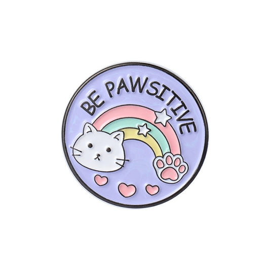 un pin's rond au design d'un adorable chat et d'un arc-en-ciel et d'une patte de chat. Le message Be Pawsitive y est inscrit. En plus du jeu de mot, il véhicule un message positif qui fait du bien au moral