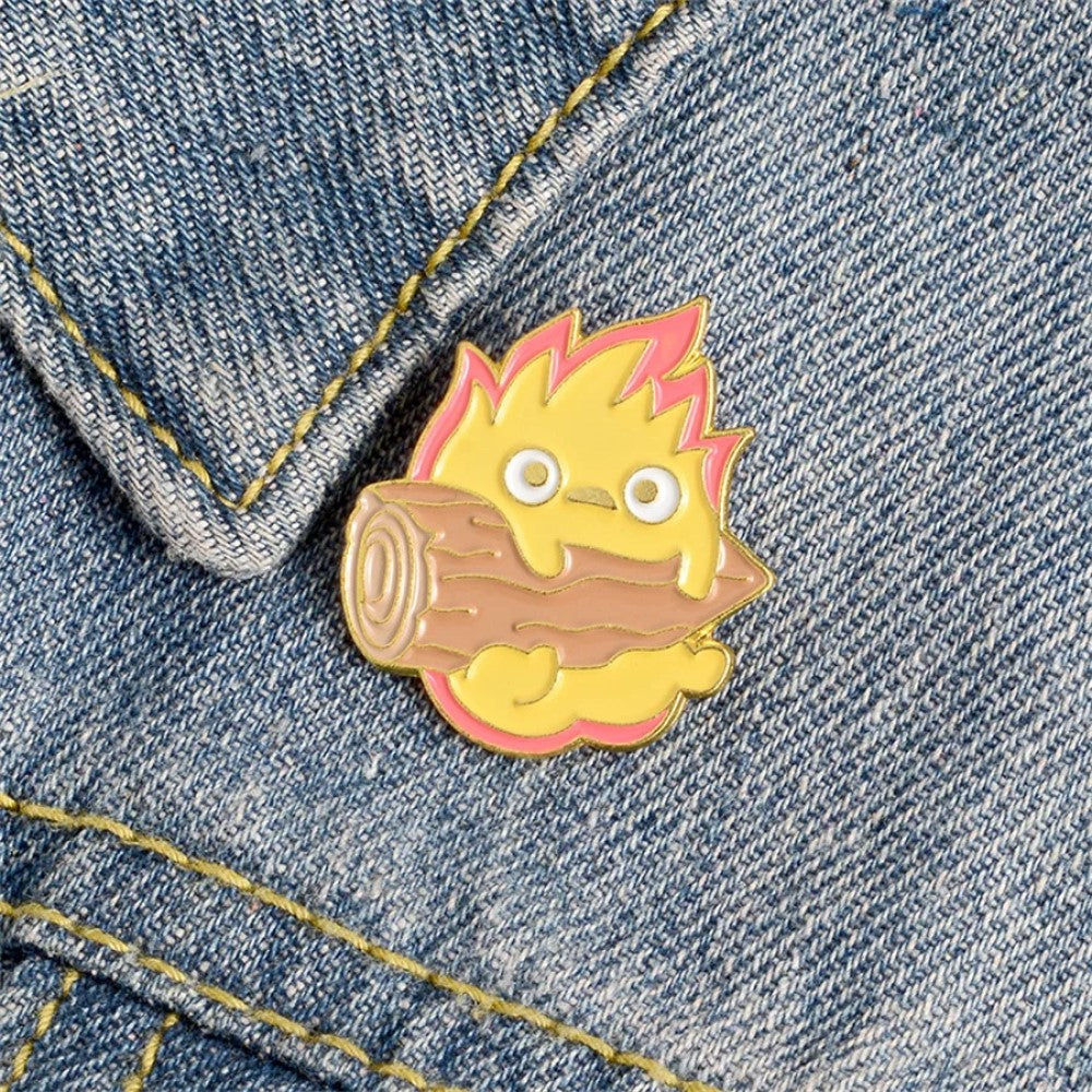 un adorable pin's représentant Calcifer le personnage du château ambulant tenant une buche de bois sur une veste en jeans. Détail mignon et touche kawaii assuré. Idéal à collectionner.