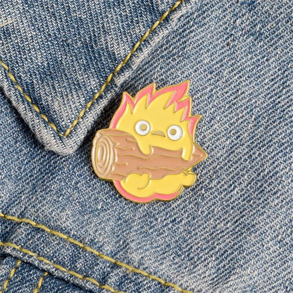 un adorable pin's représentant Calcifer le personnage du château ambulant tenant une buche de bois sur une veste en jeans. Détail mignon et touche kawaii assuré. Idéal à collectionner.