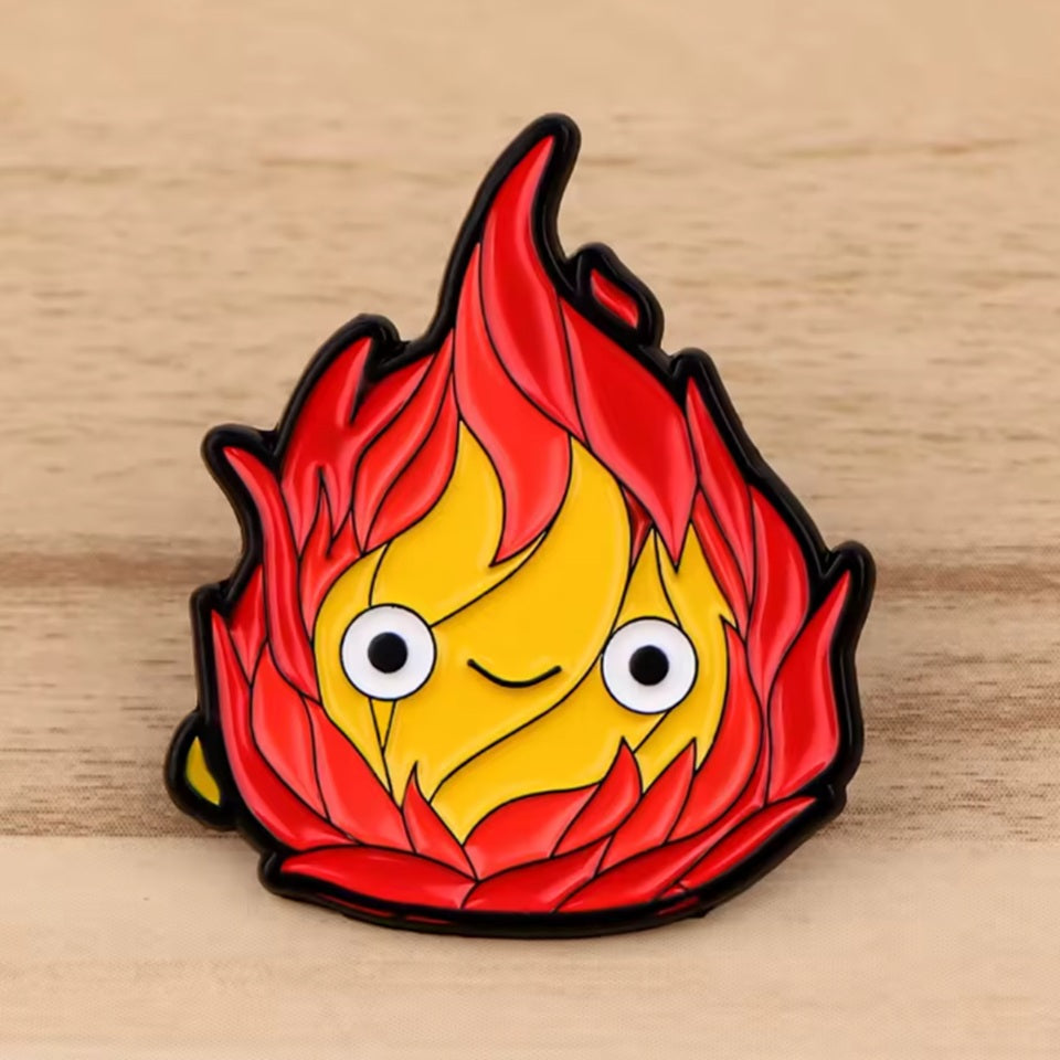un adorable pin's en forme de calcifer du château ambulant. Expression du visage souriante et trop kawaii. 