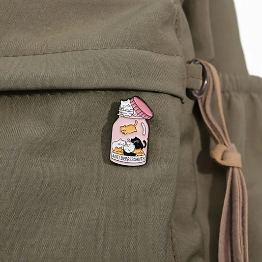 un pin's en forme de bocal dans lequel se trouve plein de petits chats colorés. Sur la boite est inscrit antidepressants, comme si les petits chats étaient un remède contre la morosité