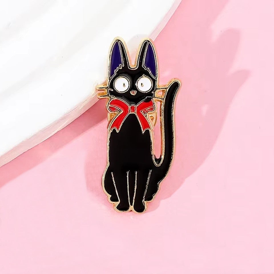 un pin's représentant Jiji, le chat noir de Kiki la petite sorcière. Avec son noeud rouge et ses oreilles violettes, il est un personnage plein de charisme et de charme.