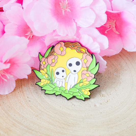 un joli pin's représentant des kodamas, petits êtres mystérieux de la fôret. ils sont dans un décor fleuri et nature