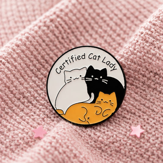 un pin's rond représentant trois petits chats blanc, roux et noir blottis les uns aux autres. Un texte les accompagne : certified cat lady. Pour un style assumé, humoristique et mignon à la fois