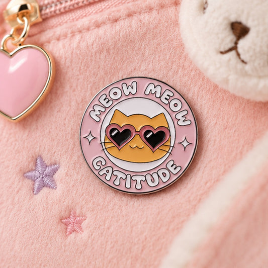 un adorable pin's rond représentant un chat orange à lunettes en forme de coeur. Il représente la catitude nonchalante et mignonne à la fois !