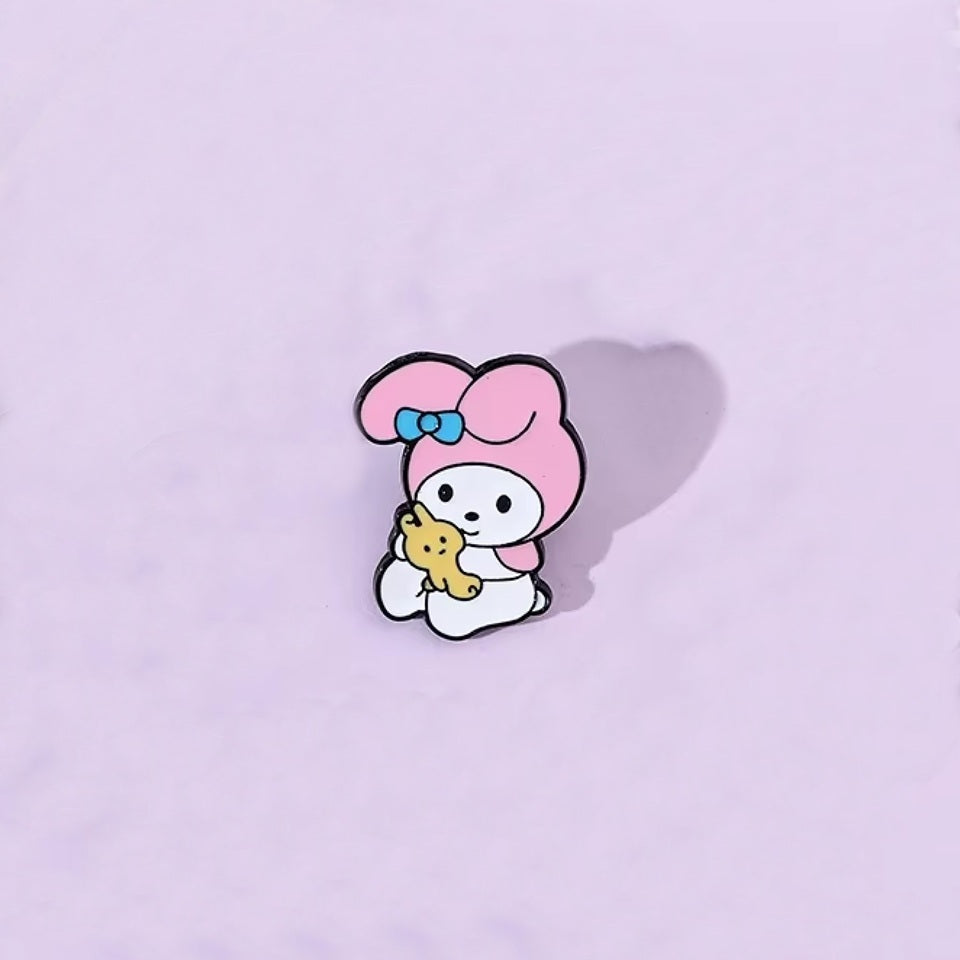 un pin's au design du personnage My Melody de Sanrio. Identifiable grâce à ses longues oreilles roses, il est ici dans une pose trop mignonne avec un petit ourson en peluche dans les mains.